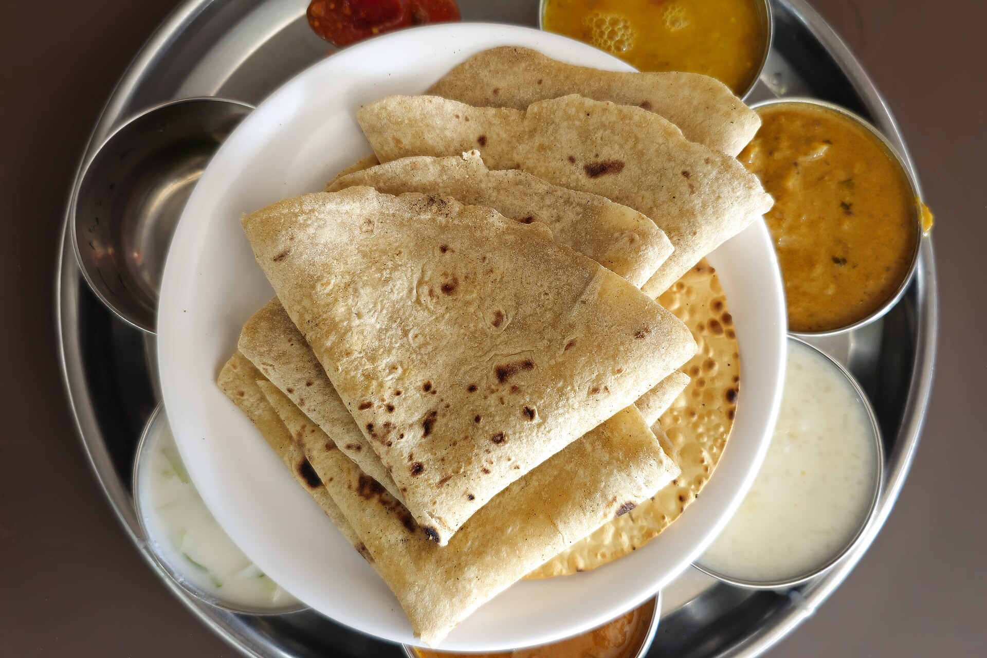 A round vegetarian thali of rotis with small bowls of dal, curries and curd