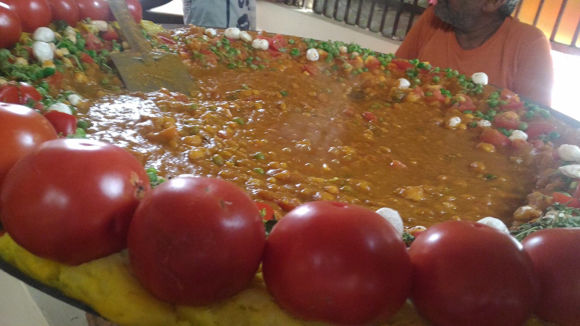 A wide iron pan of tamatar chaat ringed with whole tomatoes, as Banarasi chaat sellers cook it