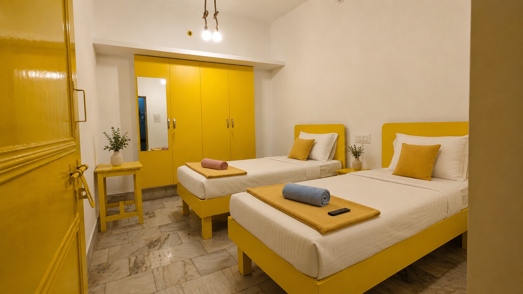 Gardenia, Varanasi: twin room with two yellow beds, folded towels on each, a mirrored yellow wardrobe and a pendant pair of bulbs on rope flex