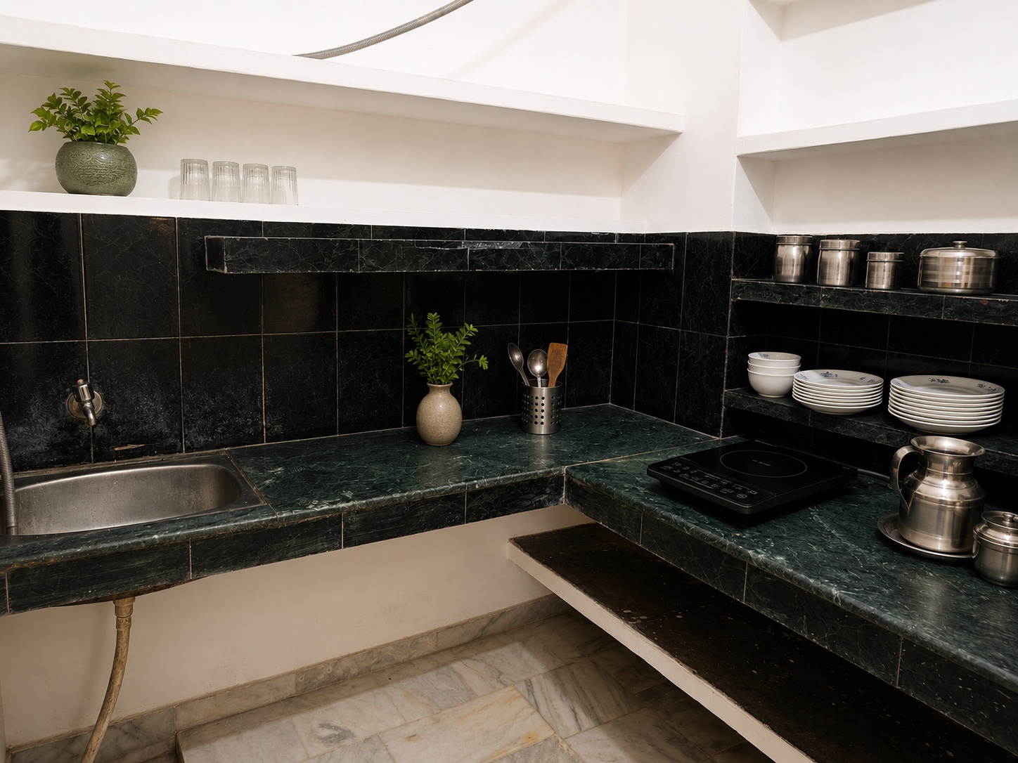 Gardenia, Varanasi: green marble kitchen counter with a steel sink, induction hob, stacked white crockery and steel storage tins on open shelves
