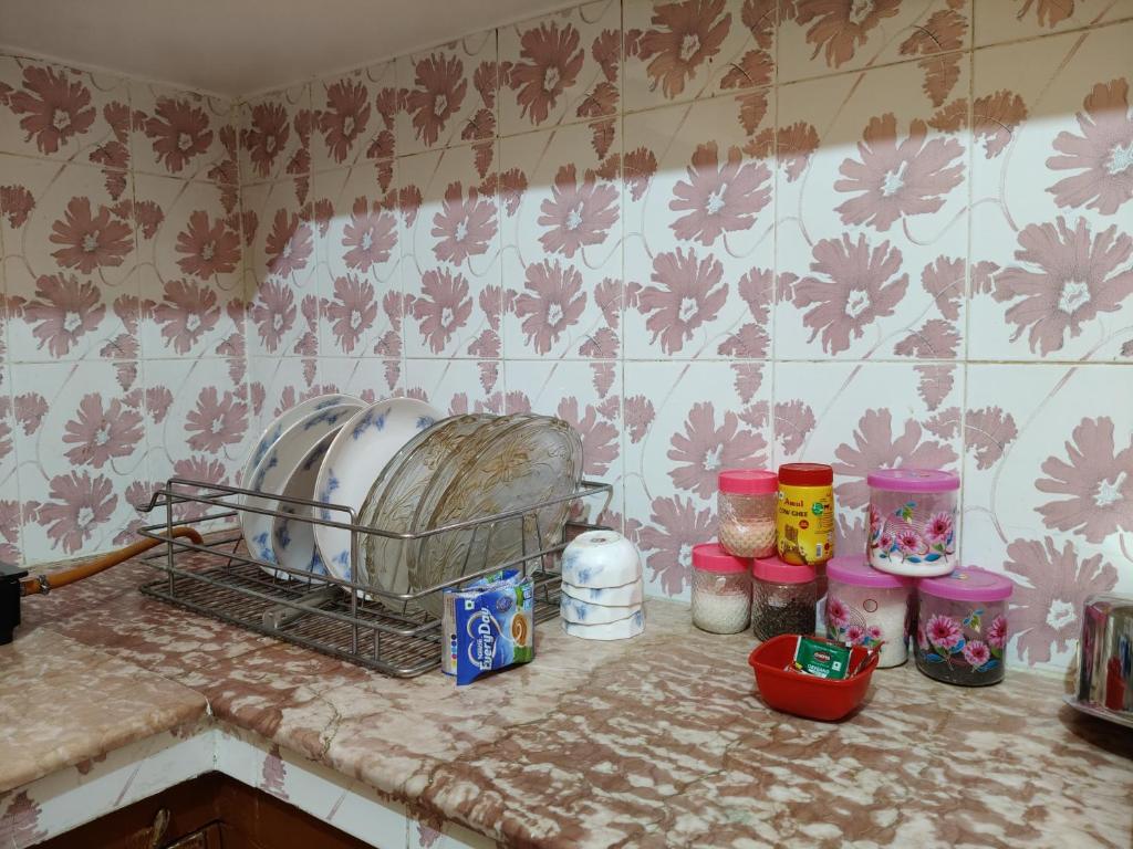 Pratham, Varanasi: kitchen counter with plates and serving dishes draining in a steel rack, spice and pulse jars lined up against a floral-tiled wall
