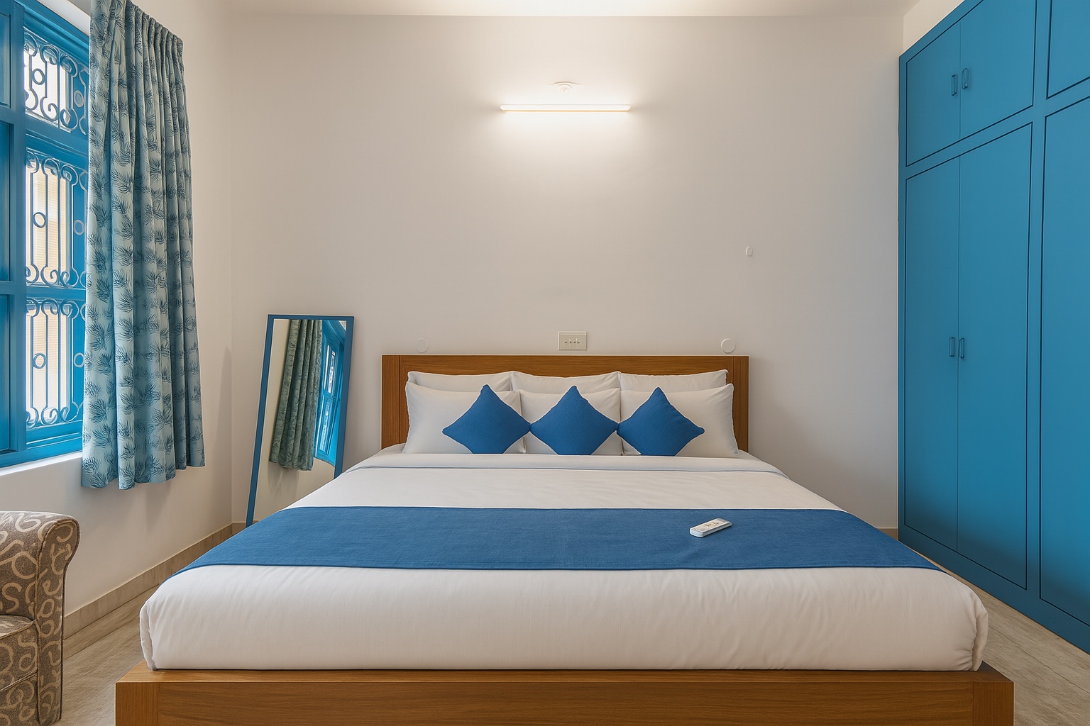 Santorini, Varanasi: bed seen head-on with three blue cushions, a blue fitted wardrobe to one side and a leaning mirror by the curtained window