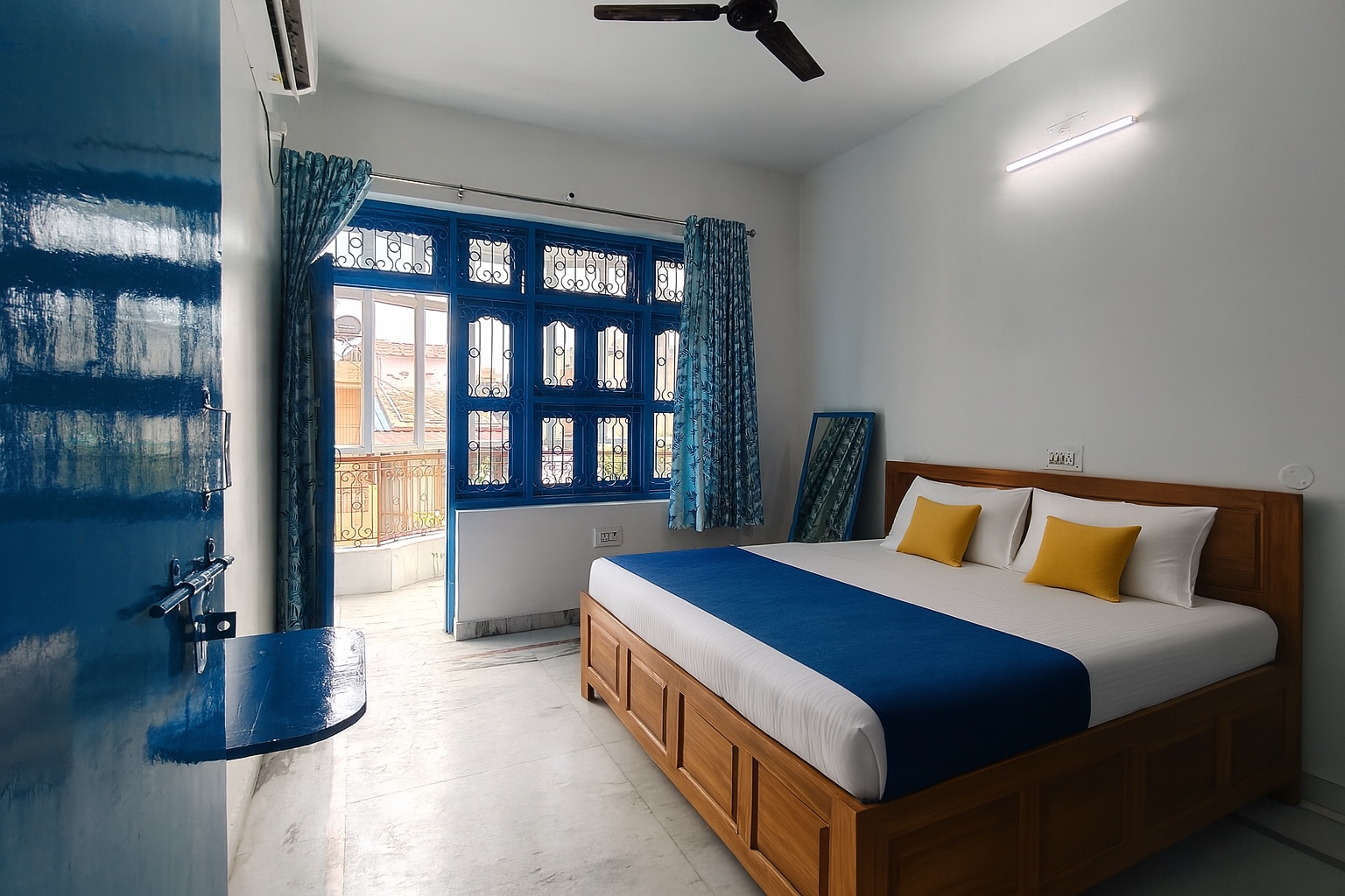 Santorini, Varanasi: corner room with blue shutters folded back from a balcony over the rooftops, teak bed with mustard cushions and a blue wall table