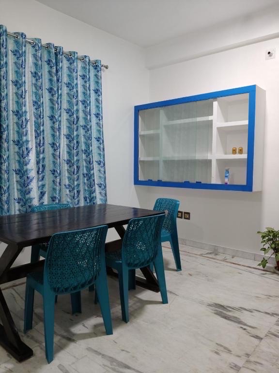 Santorini, Varanasi: shared dining area with a dark table and blue moulded chairs beneath a blue-framed wall cabinet, leaf-print curtains at the window