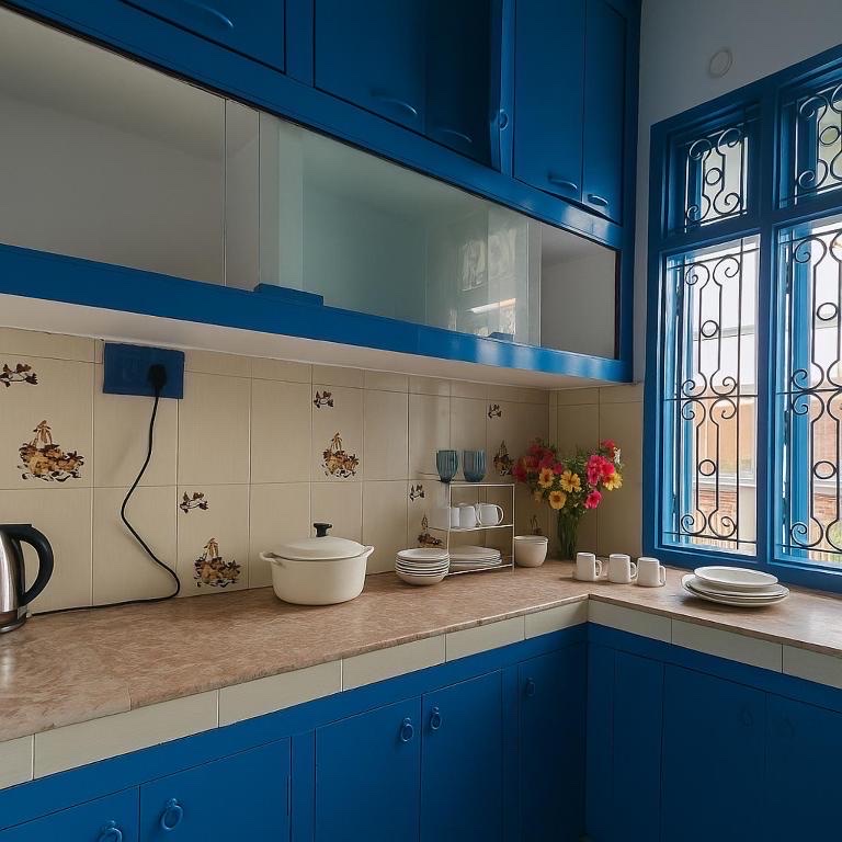 Santorini, Varanasi: blue-cabinet kitchen corner with a casserole dish, mugs and plates on the counter, fresh flowers by the blue-framed barred window