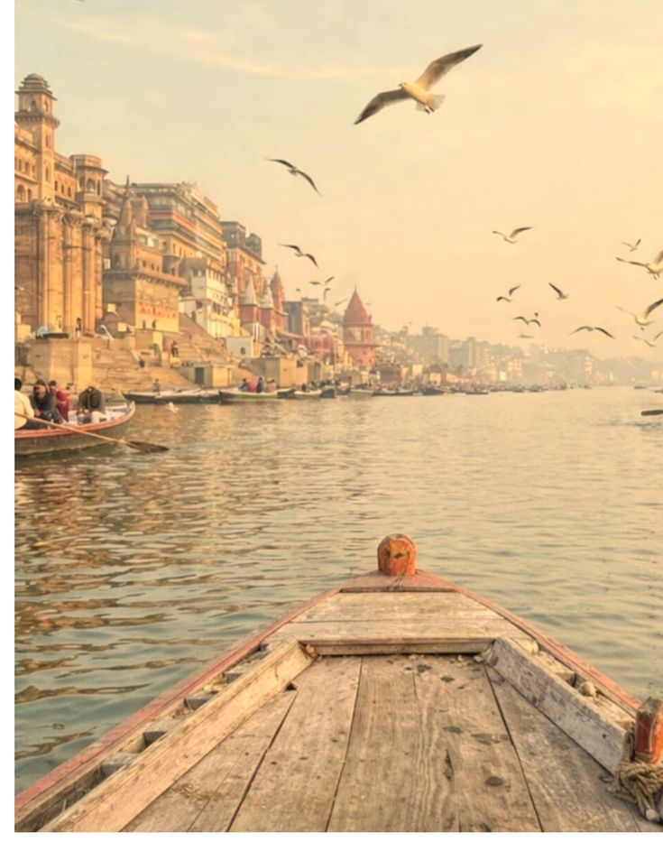 A wooden boat on the Ganga at first light, the ghats and their buildings catching the sun